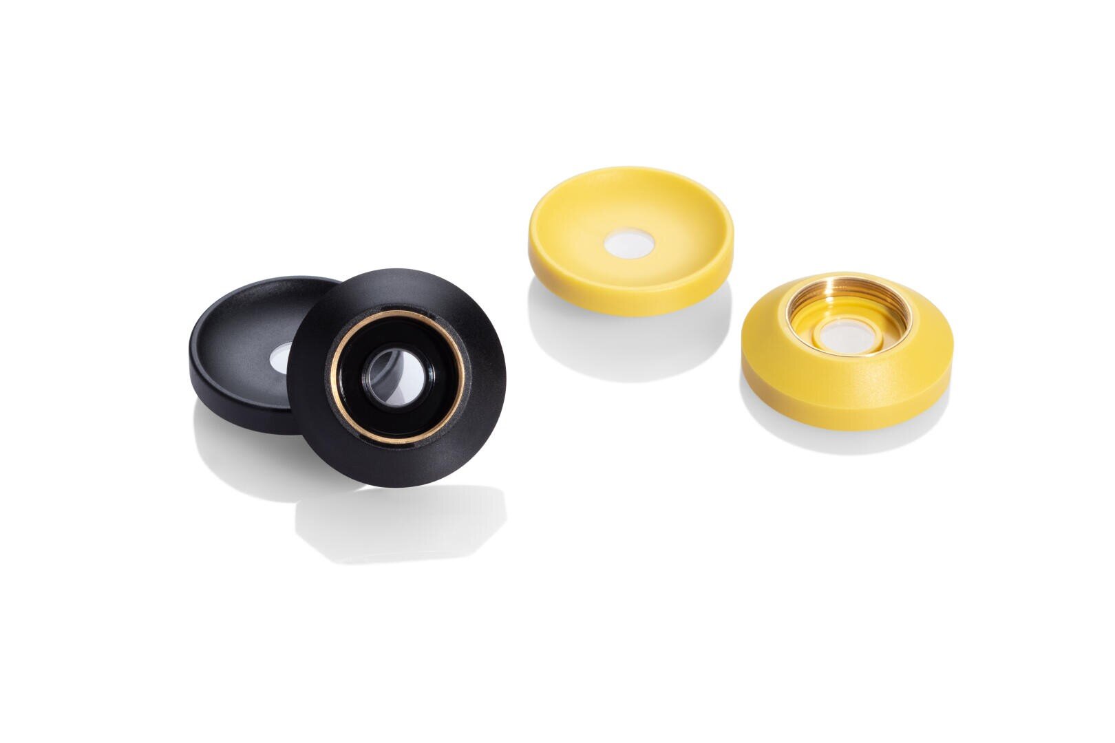 Four circular objects, two black and two yellow, each with a metallic ring or center, are arranged on a white background. The objects appear to be small mechanical or electronic components.