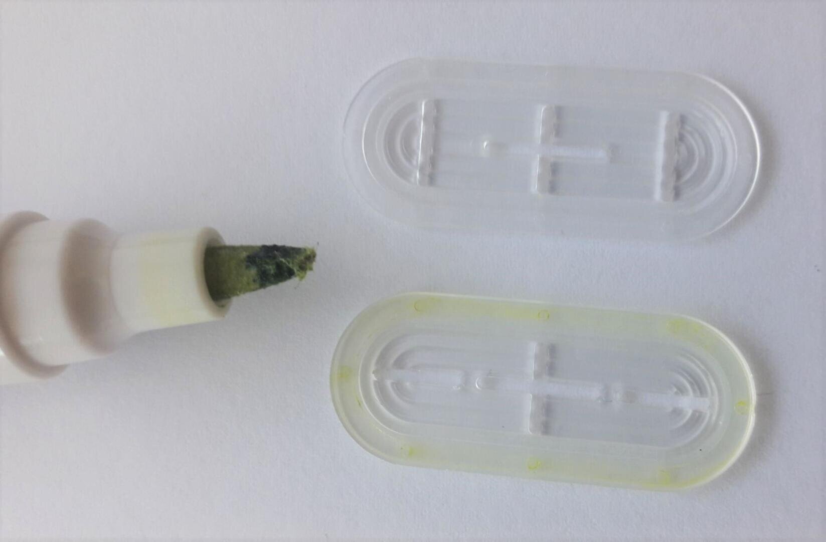 Close-up of a marker with an exposed green tip next to two transparent plastic caps lying on a white surface.