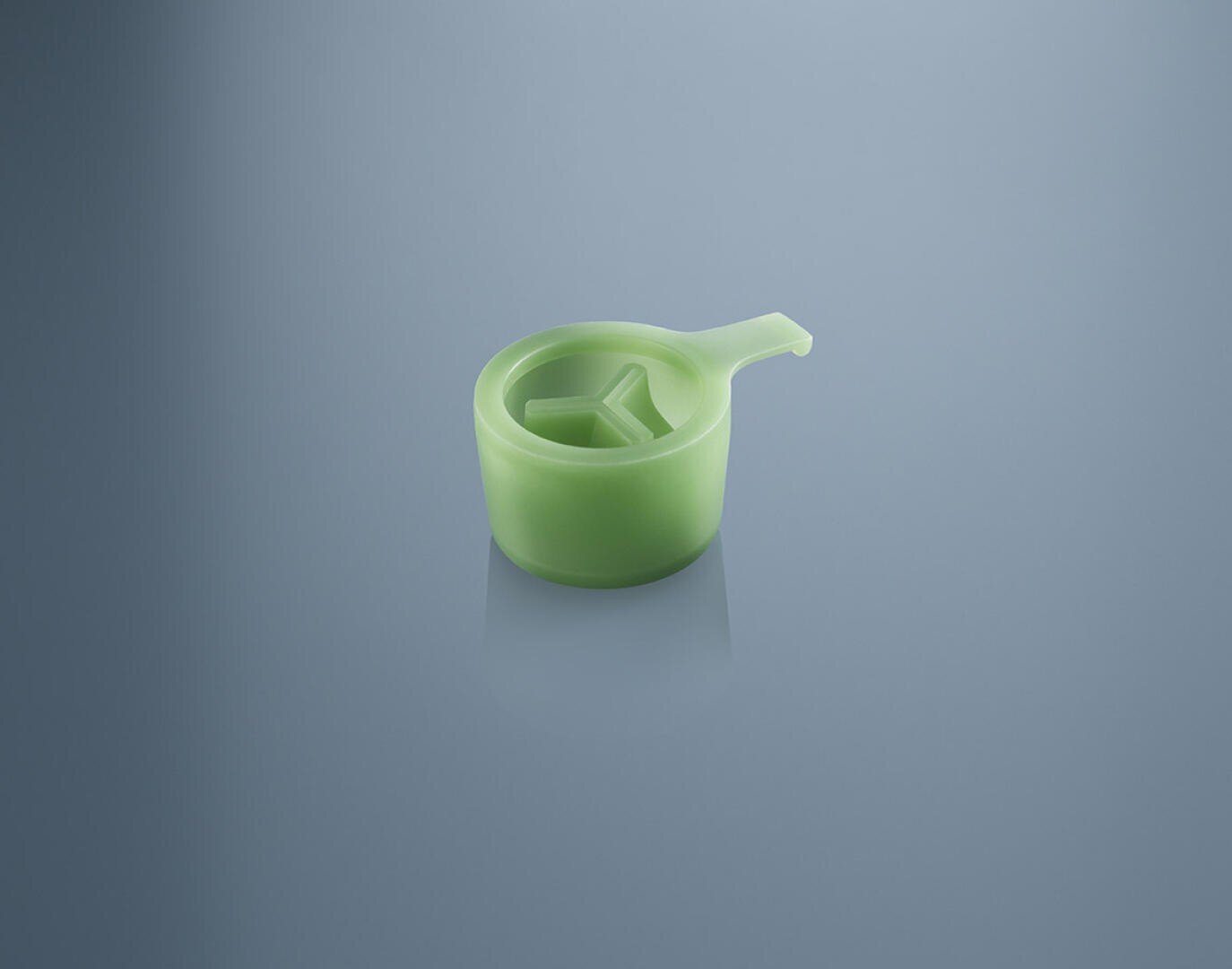 A small, green plastic object with a handle and three inner compartments sits on a reflective blue surface.